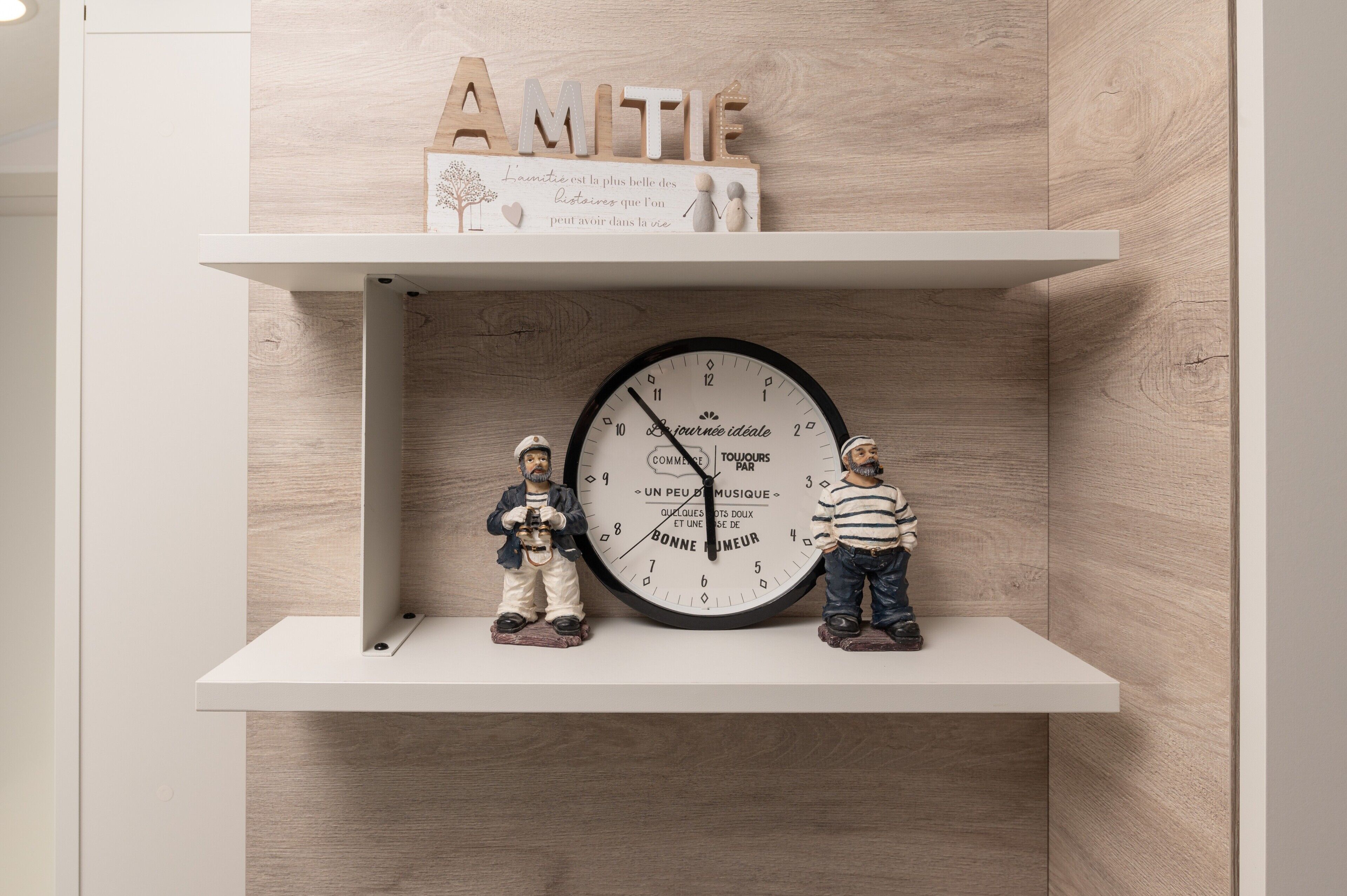A clock with French text, two figurines, and wooden letters spelling 'AMITIE' on a shelf.