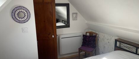 A bedroom with a bed, a chair, a wooden door, a mirror, and a wall-mounted radiator.
