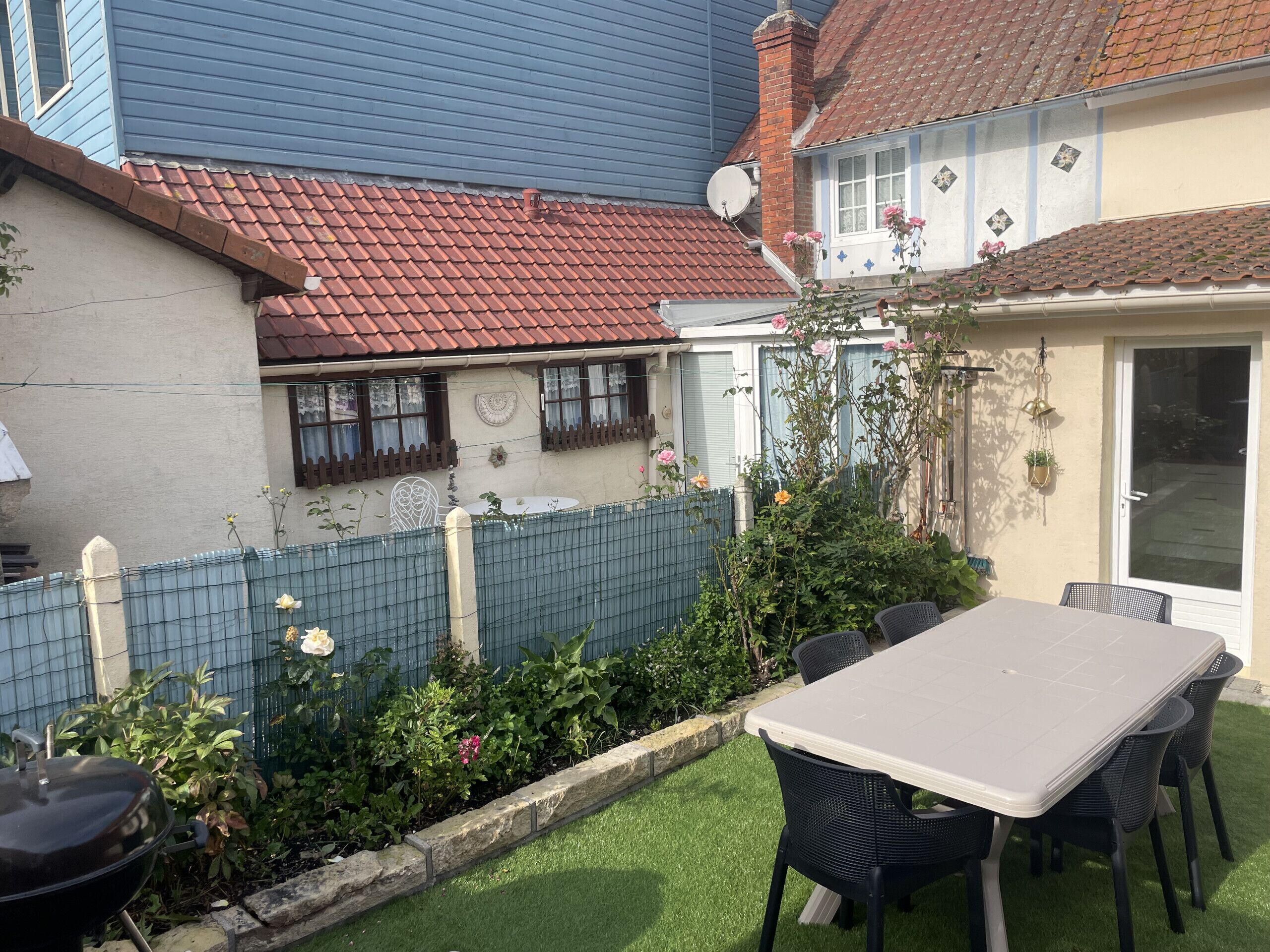 A patio area with a table and chairs, surrounded by a garden with various plants and flowers.