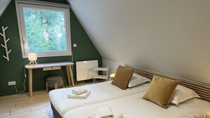 Ein Schlafzimmer mit einem großen Bett, zwei Kissen, einem Schreibtisch mit Stuhl und einem Fenster mit Blick auf Bäume.
