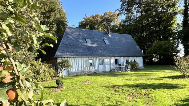 Ein Haus mit geneigtem Dach, einer kleinen Veranda mit Stühlen und einem gepflegten Rasen.