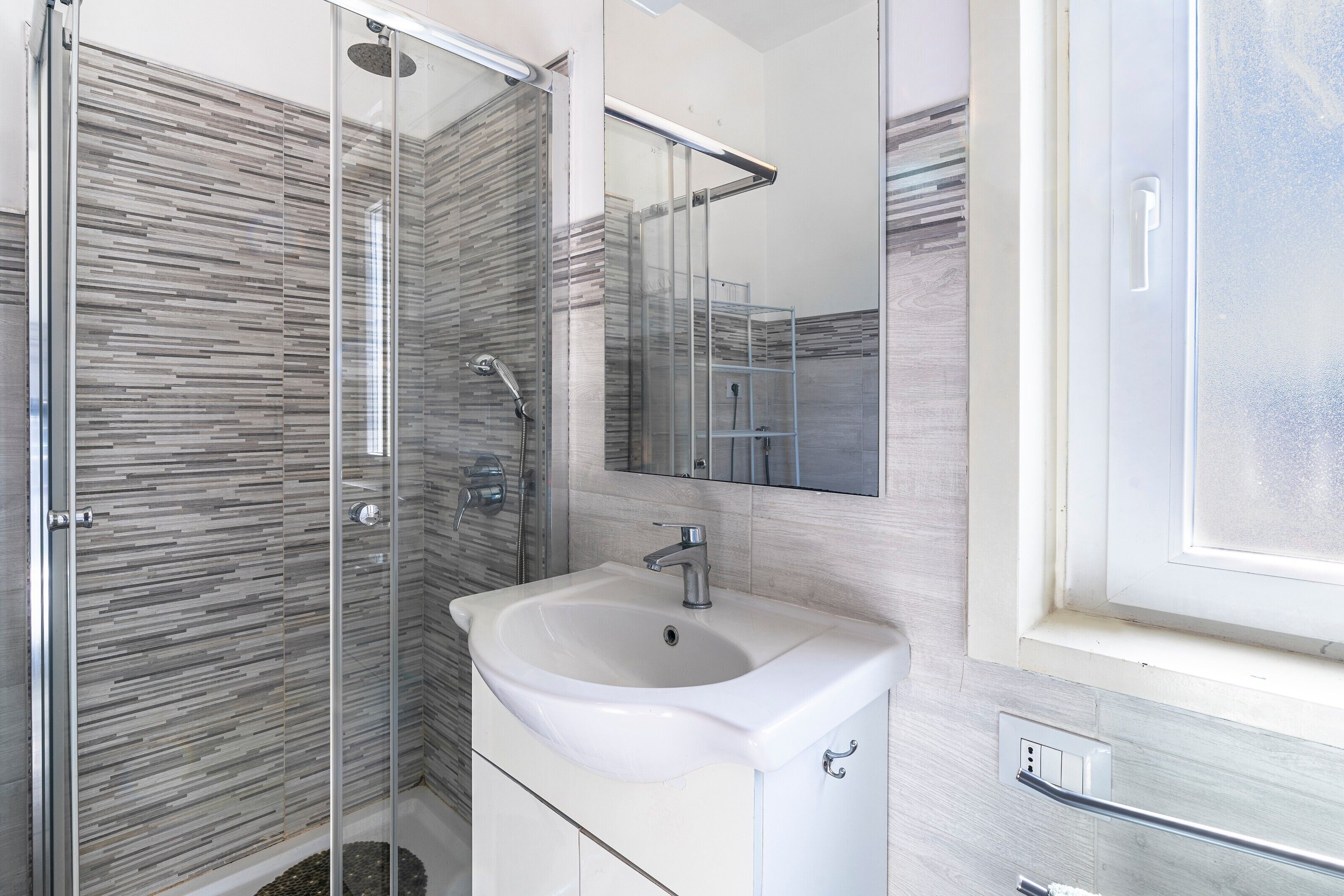 A modern bathroom with a glass shower enclosure, a white sink, and a mirror above it.