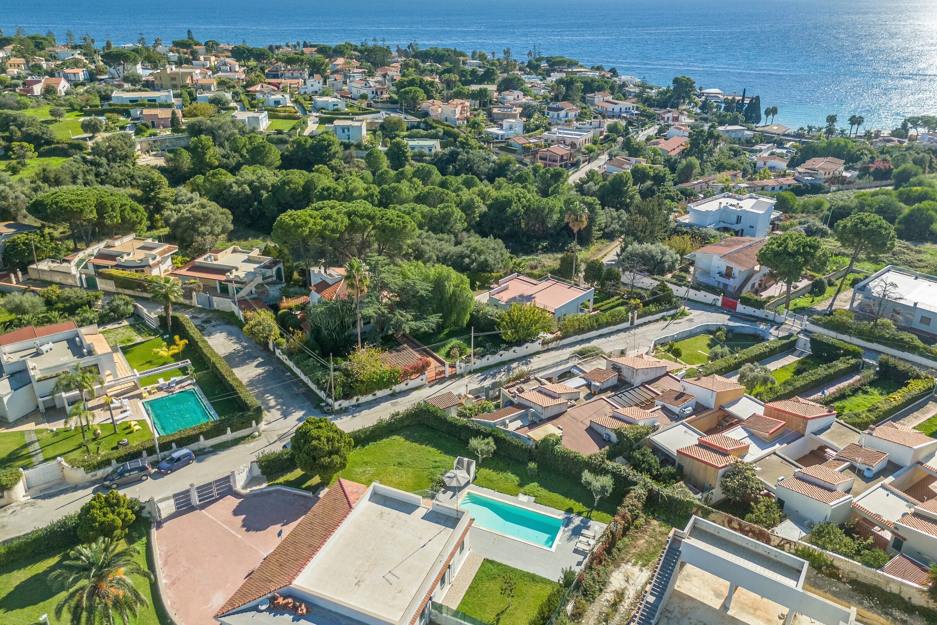 An aerial view of a residential area with houses, a swimming pool, and a clear view of the sea.