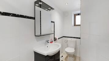 Un baño con un lavamanos blanco, un espejo con iluminación, un inodoro y una ventana.