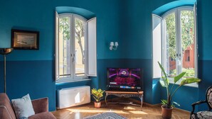 A living room with teal walls, a television, a radiator, a potted plant, and a patterned rug. - Bohémien Rome (Roma)