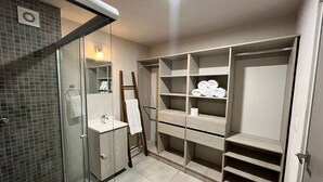 Ein modernes Badezimmer mit Duschkabine aus Glas, Waschtisch mit Spiegel und integriertem Stauraum mit Regalen und Schubladen.