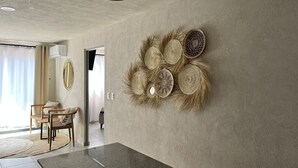 Ein modernes Interieur mit Betondecke, einem großen gewebten Wandkunstwerk, einem Essbereich mit Tisch und Stühlen sowie einem großen Fenster mit Vorhängen.