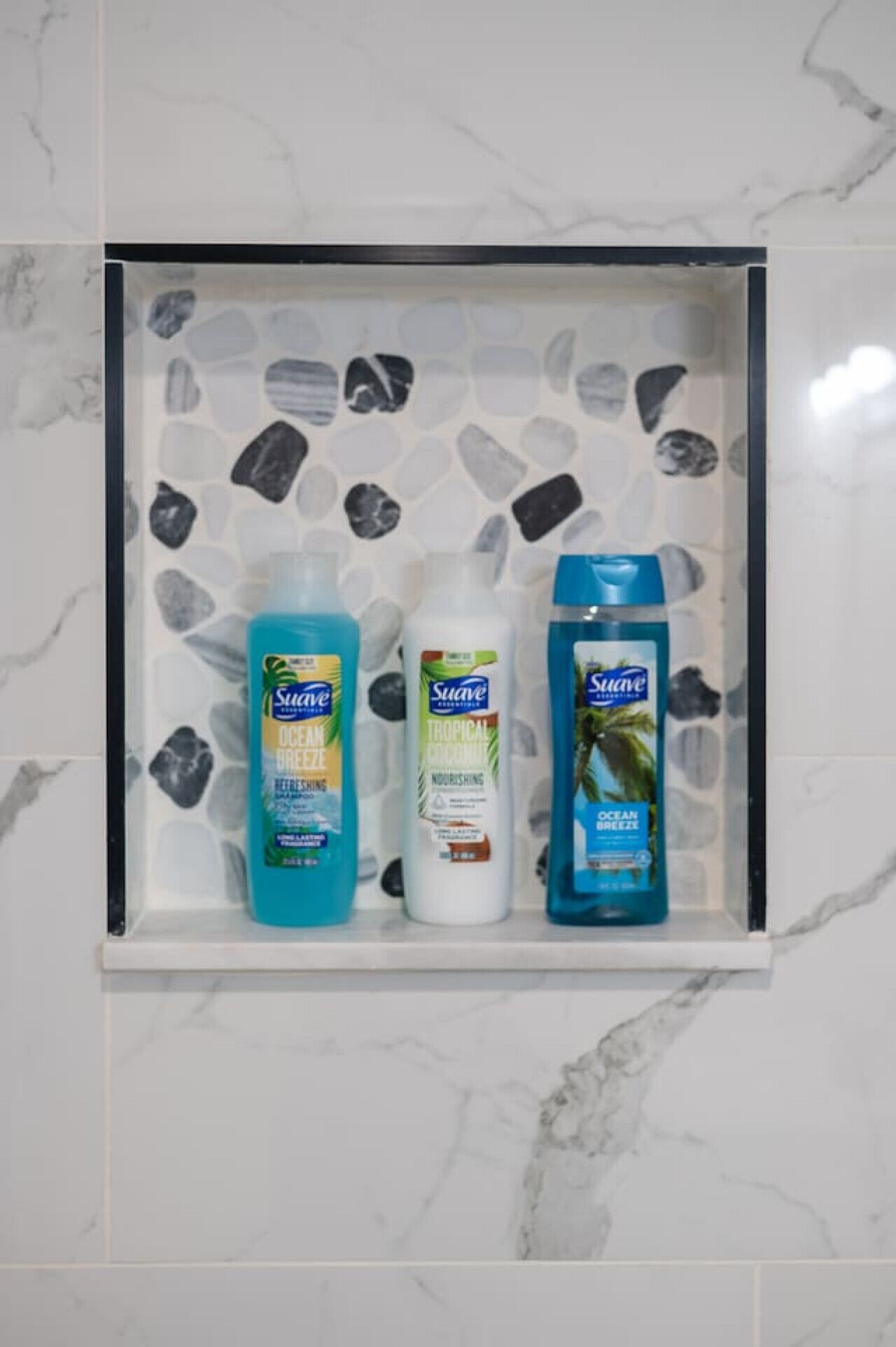 Un estante de baño con tres botellas de productos Suave para el cuidado corporal.