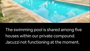 En swimmingpool omgiven av frodig grönska och palmer, med en pergola och ett utomhusområde med sittplatser.