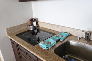 A kitchen with a black induction cooktop, a stainless steel sink, and two teal kitchen towels with a tropical design.