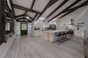 A modern kitchen with white cabinetry, a large island with bar stools, and a dark wooden ceiling. - Entire Home+Pool+Ping Pong Table+Arcade (Kissimmee)