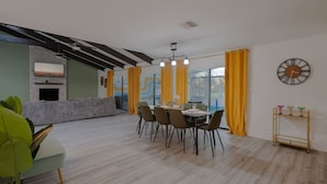 En moderne stue med spiseplads, pejs og et stort vindue med gule gardiner.