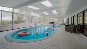 En indendørs swimmingpool med glasvægge, flisegulv og et par liggestole.