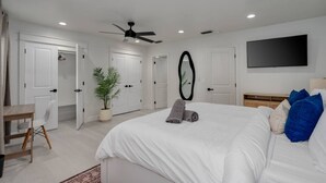 A modern bedroom with a large bed, a ceiling fan, a TV, and white walls. - Lakefront Mansion with Pool and Pilates (Orlando)
