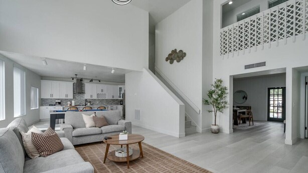 A spacious living area with a grey sofa, a coffee table, and a dining area in the background. - Lakefront Mansion with Pool and Pilates (Orlando)