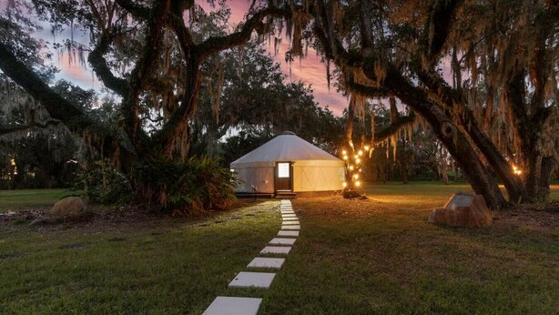 A yurt with a thatched roof, surrounded by trees with hanging moss, and a stone pathway leading to the entrance. - Florida Yurt Escape • Nature + Comfort (Kissimmee)