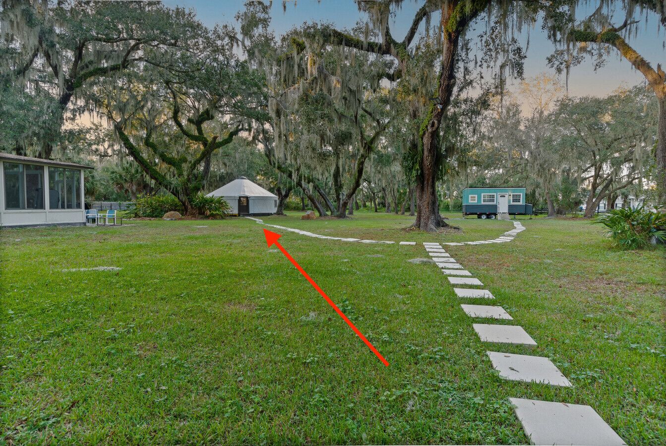 Uma área gramada com um edifício branco, uma casa móvel azul e um caminho que leva a um gazebo.