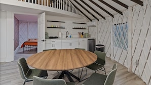 A dining area with a round wooden table and four chairs, a kitchen with white cabinets and a black countertop, and a staircase leading to an upper level. - Florida Yurt Escape • Nature + Comfort (Kissimmee)