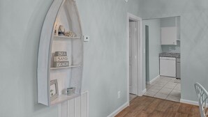 A hallway with a wooden floor, a white door, and a kitchen area with a white dishwasher and a granite countertop. - A Seaside Serentiy in Morehead City (Morehead City)