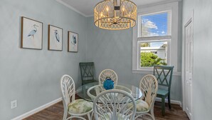 A dining area with a round glass table, white chairs, a blue vase, and framed bird paintings on the wall. - A Seaside Serentiy in Morehead City (Morehead City)