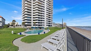 Un hotel de altura con piscina, sillas de descanso y vista al mar.