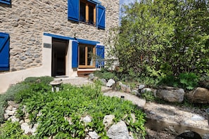 A stone building with blue shutters, a stone pathway, and a garden area. - Studio Apartment 'Sorbier Des Oiseaux' with Mountain View, Private Terrace and Wi-Fi (Font-Romeu-Odeillo-Via)