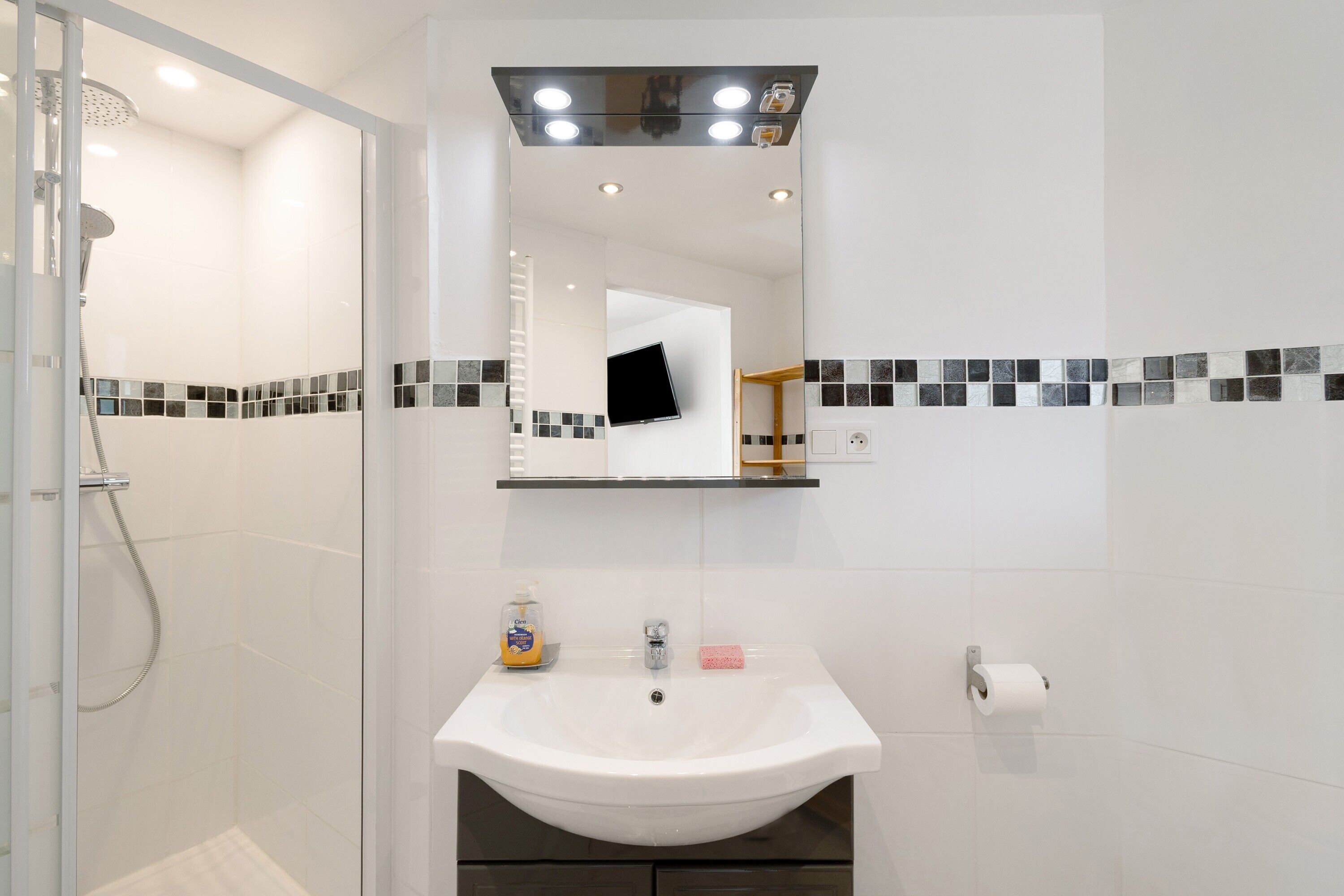 Un baño con ducha, lavamanos, espejo y paredes con azulejos.