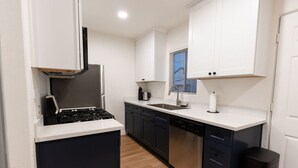 A compact kitchen with dark cabinets, a white countertop, a stove, a sink, and a window with blinds.