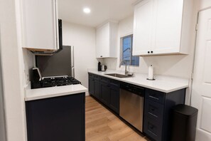 A compact kitchen with dark cabinets, a white countertop, a stove, a sink, and a window with blinds. - Modern Hideaway in North Park - 3941 (San Diego)