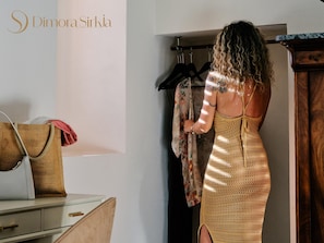 A woman in a yellow dress standing in a room with a wooden wardrobe, a white wall, and a hanging garment.