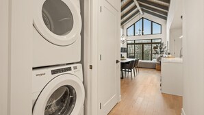 Une buanderie équipée de deux lave-linge Whirlpool, un coin repas avec une table et des chaises, et une vue sur une grande fenêtre et un escalier menant à l’étage supérieur.