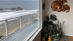 A balcony with a view of the beach and ocean, a wooden octopus wall decoration, and various potted plants. - Surfers Perch: Amazing Pacific Ocean Views (Tillamook)