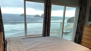 A bedroom with a large window overlooking a beach and ocean. - Surfers Perch: Amazing Pacific Ocean Views (Tillamook)