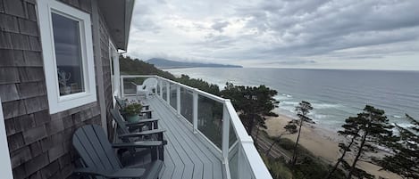 A wooden deck with outdoor furniture overlooking a beach and ocean.