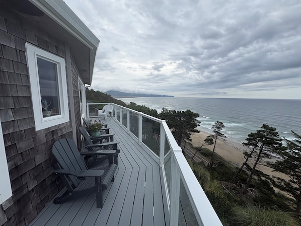 A wooden deck with outdoor furniture overlooking a beach and ocean.