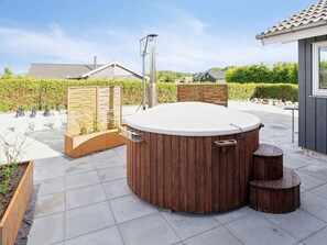A hot tub with wooden panels and a metal structure in a landscaped outdoor area.