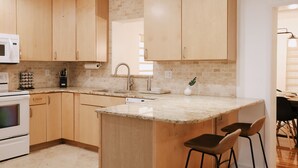 A modern kitchen with wooden cabinets, a built-in microwave, and a granite countertop. - 3 miles to Siesta Key, Screened in Lanai, 3 Bedrooms, Walking dist to Publix (Sarasota)