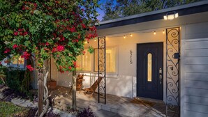 A modern house with a dark blue door, a porch with two chairs, and a garden with red flowers. - 3 miles to Siesta Key, Screened in Lanai, 3 Bedrooms, Walking dist to Publix (Sarasota)