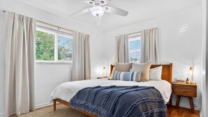 A bedroom with a bed, wooden headboard, bedside tables, a ceiling fan, and large windows with curtains. - 3 miles to Siesta Key, Screened in Lanai, 3 Bedrooms, Walking dist to Publix (Sarasota)