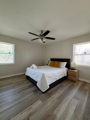 A bedroom with a bed, a nightstand, a ceiling fan, and two windows with blinds.