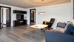 Ein modernes Wohnzimmer mit Holzboden, einem runden Tisch, einer Couch und einem Fernseher auf einer schwarzen Kommode.