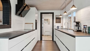 Eine moderne Küche mit weißen Schränken, einer Holz Arbeitsplatte, Pendelleuchten und Blick in den angrenzenden Wohnbereich.