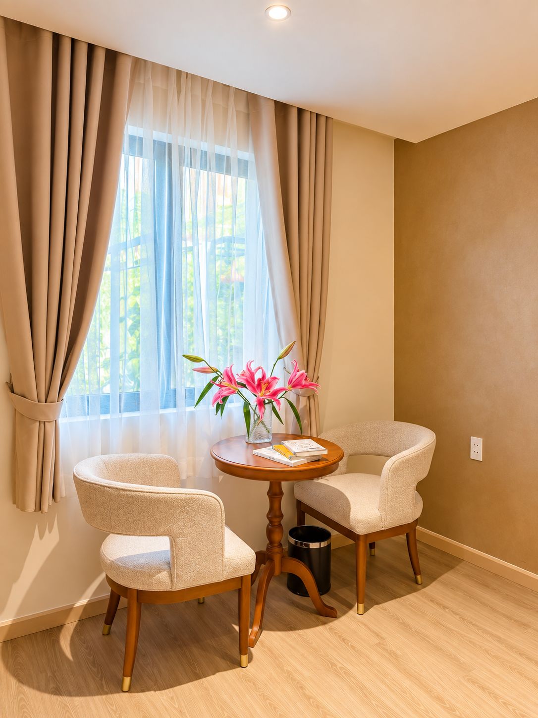 A room with two chairs, a small round table, a vase with flowers, and a window with curtains.