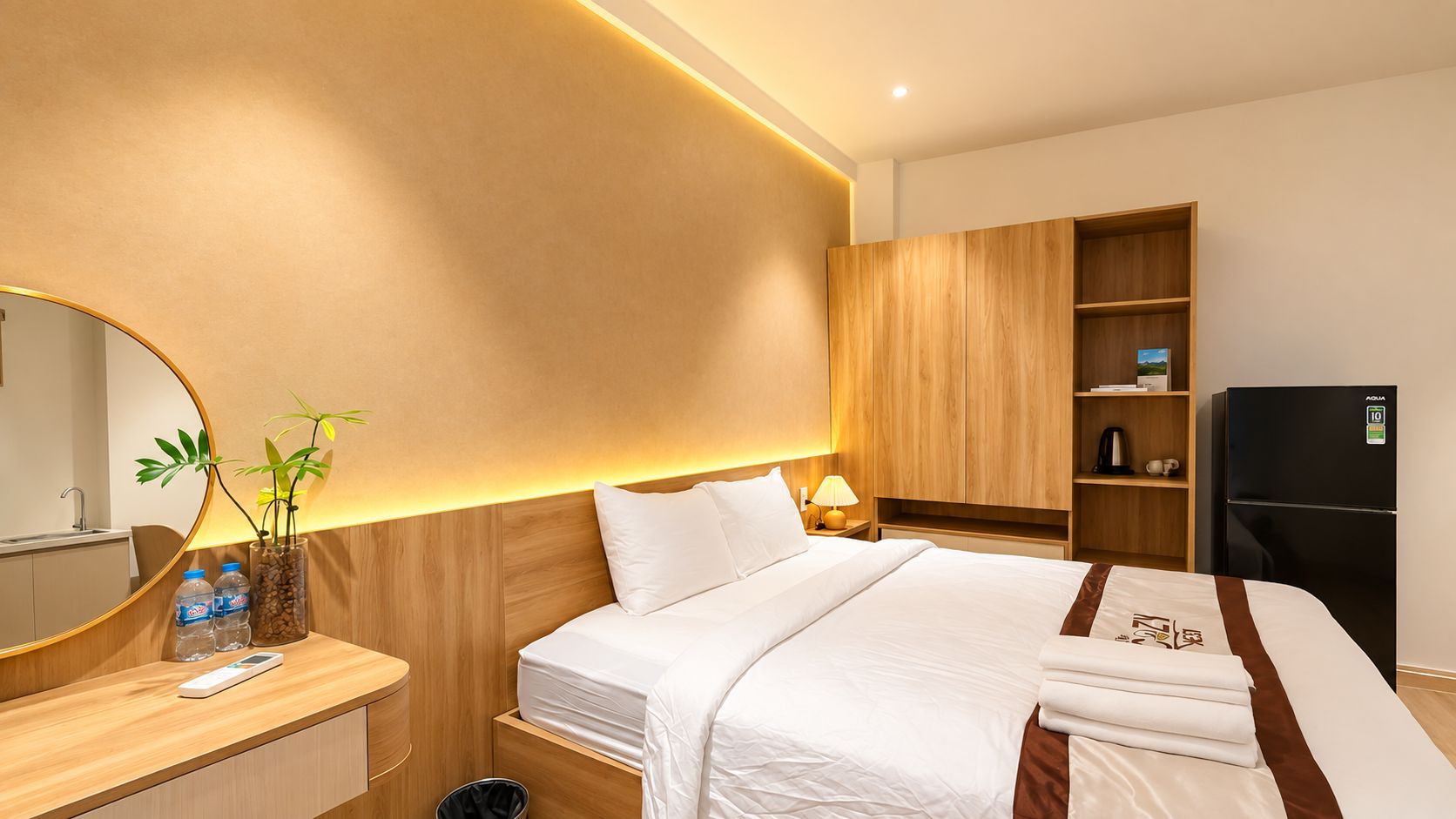 Camera d'albergo con un letto, un armadio in legno, un frigorifero nero, un comodino con una lampada e uno specchio.