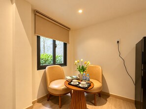 A room with two leather chairs, a small wooden table with a tray of cups and water bottles, and a window with a view of greenery. - Chinchu Stay  (Ho Chi Minh City)