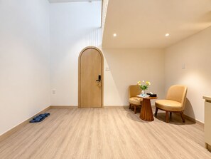 A room with a wooden door, a small round table with a vase of flowers, two chairs, and a pair of slippers on the floor. - Chinchu Stay  (Ho Chi Minh City)