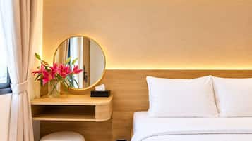 Habitación de hotel con cama, mesita de noche con espejo, jarra de flores y un taburete pequeño.
