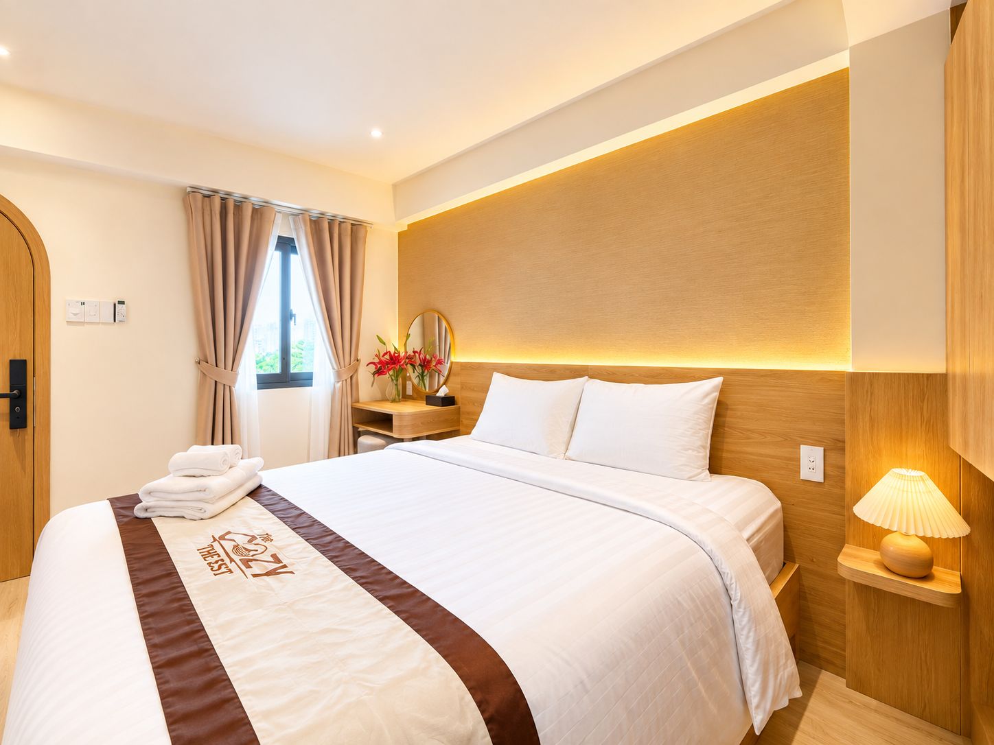 A hotel room with a neatly made bed, a bedside table with a lamp, and a window with curtains.