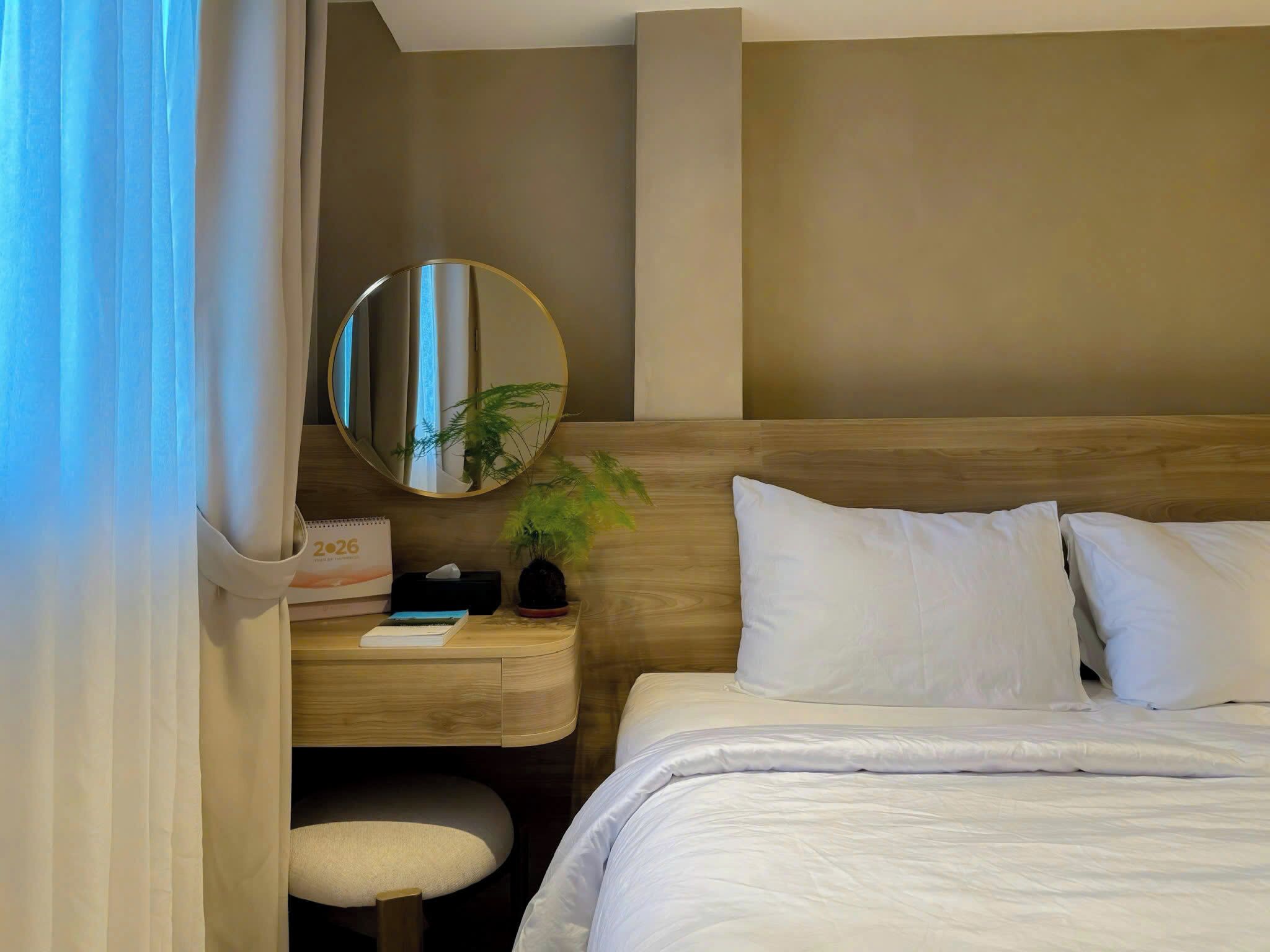 Habitación de hotel con cama, mesita de noche, espejo, planta en maceta y un calendario.