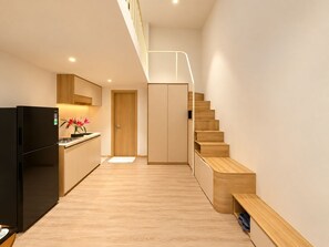 A modern kitchen with a built-in refrigerator, wooden cabinets, and a wooden staircase leading to a loft area.